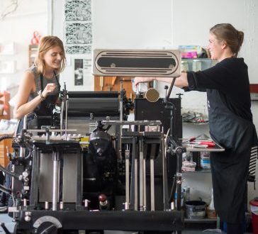 Two women working with traditional letterpress print machine in workshop